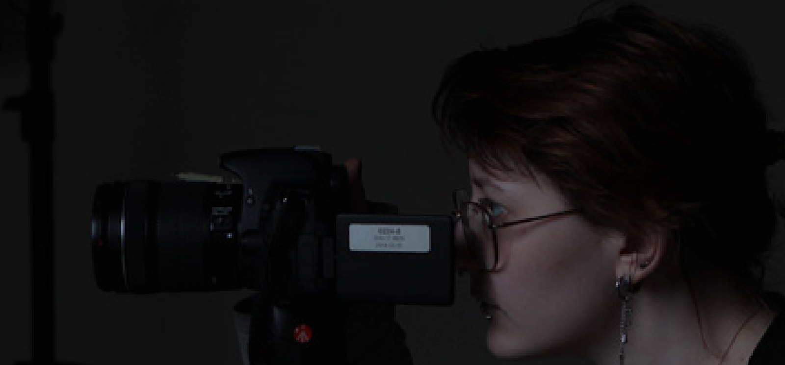 Nika in glasses looking through a camera in a dark studio
